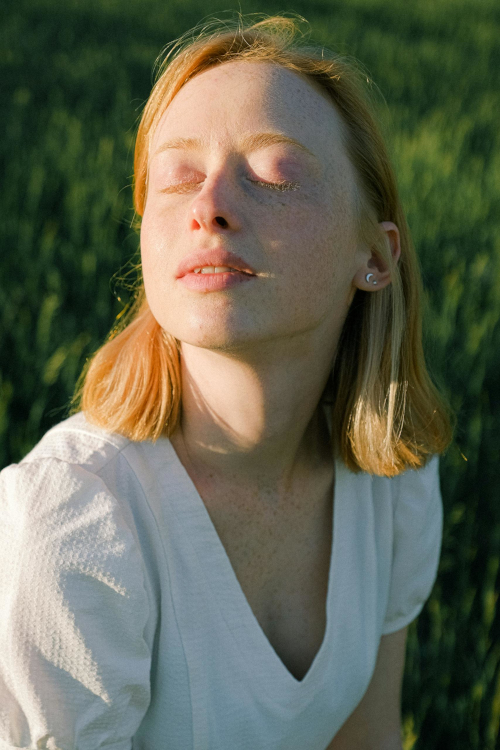 Tranquil portrait of a woman enjoying the sunlight in a grassy field.