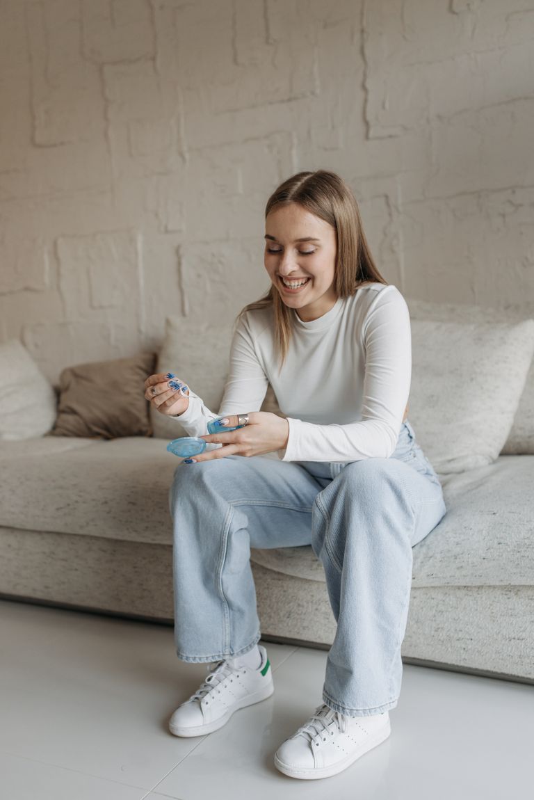 Happy woman sitting on sofa holding pH paper in a cozy living room.